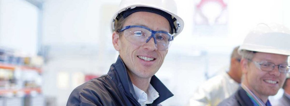 Workers in a Foundry wearing a coat, safety helmet and safety glasses. They look into the camera and look happy.