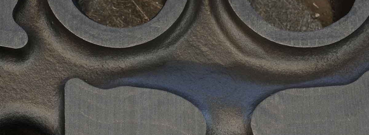 Close-up view of a foundry-cast metal part with circular cavities and a textured surface, highlighting the precision and detail in metalworking.