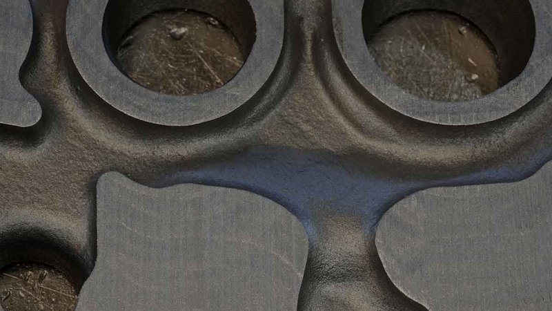 Close-up view of a foundry-cast metal part with circular cavities and a textured surface, highlighting the precision and detail in metalworking.