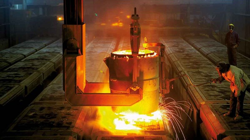 Foundry environment with intense glow of molten metal being poured, workers in protective gear ensuring precision.