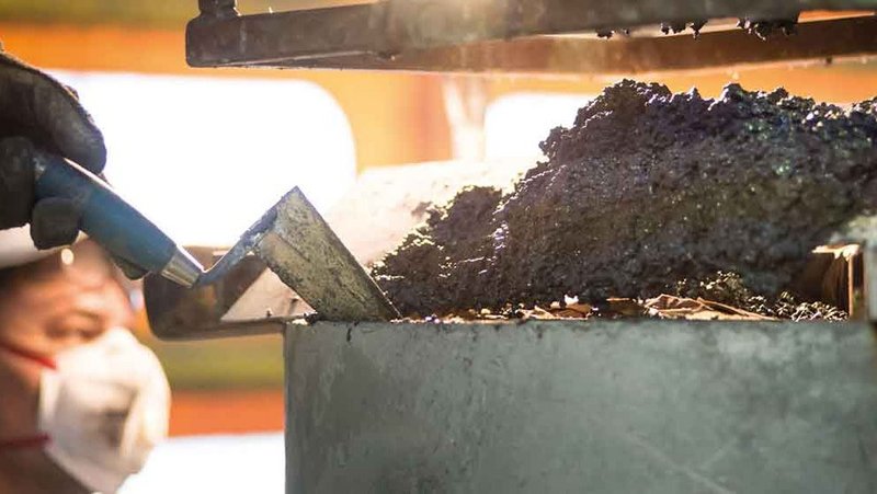 Foundry worker wearing a safety helmet and mask applying refractory material with a tool.