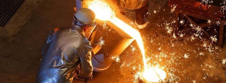 Overhead view of a foundry worker in protective gear pouring molten metal from a furnace into a mold, with bright sparks flying around the intense and fiery work environment.