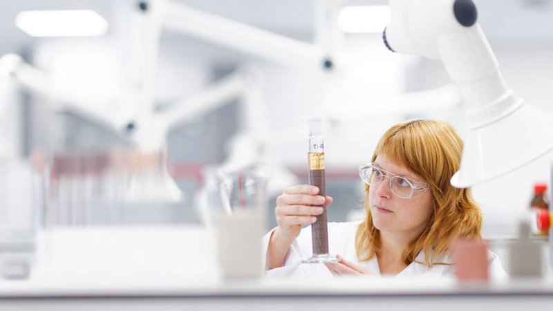 A focused laboratory technician examines a test tube filled with a coating against the light in a modern, well-equipped laboratory