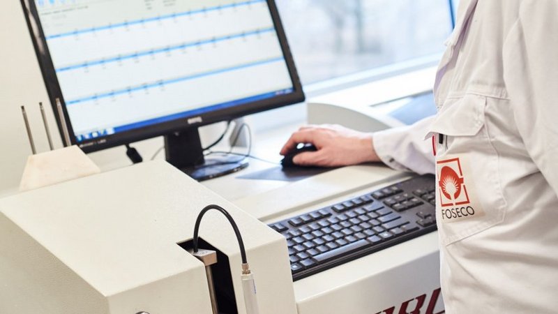 A focused technician in a lab coat operates an optical emission spectrometer, meticulously analyzing metal samples for quality control in a well-lit laboratory