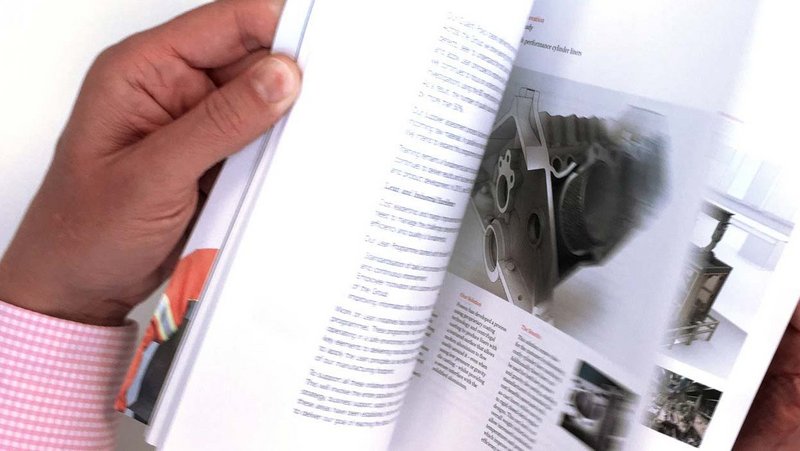 An individual flipping through a technical book on metallurgy, highlighting a detailed image of a metallic component, symbolizing continuous learning and industry expertise.