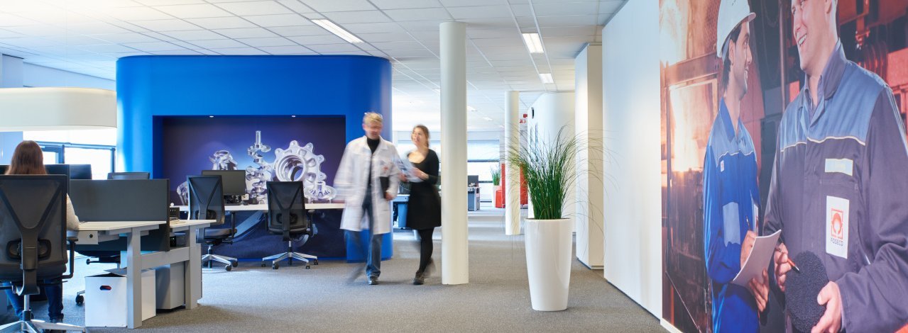 Spacious and modern office area in the R&D Centre in Enschede, featuring workstations, a blue accent wall, and life-sized wall graphics of workers in safety gear