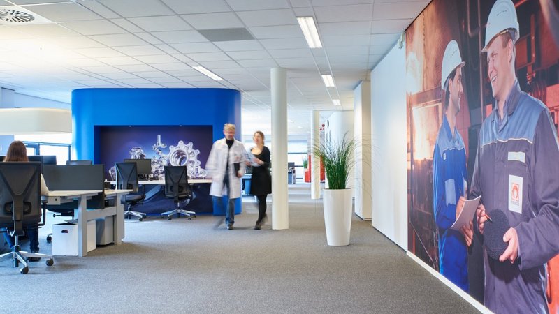 Spacious and modern office area in the R&D Centre in Enschede, featuring workstations, a blue accent wall, and life-sized wall graphics of workers in safety gear