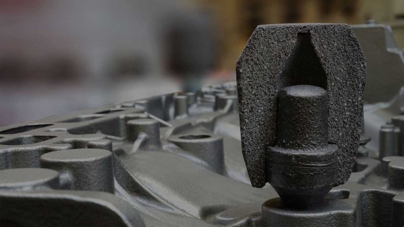 Macro view of a dark grey exothermic feeder in an industrial setting, placed on a metallic cast surface with blurred background