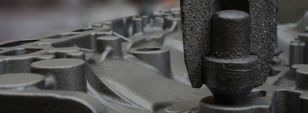 Macro view of a dark grey exothermic feeder in an industrial setting, placed on a metallic cast surface with blurred background