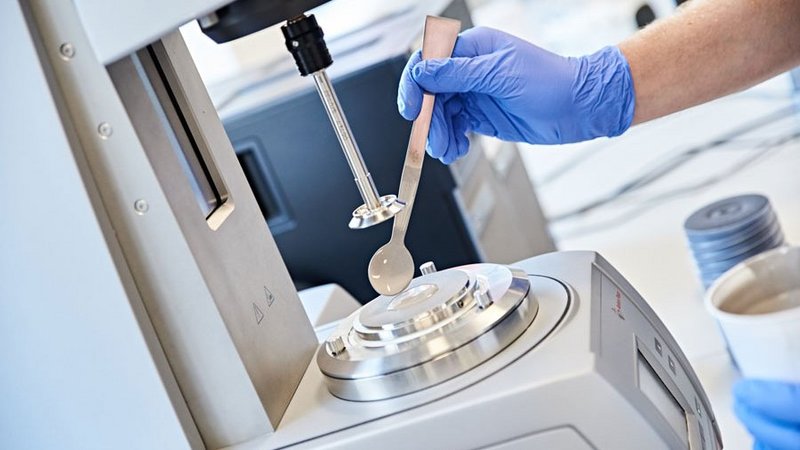 A scientist in blue gloves precisely places a sample on a rheometer platform, ensuring accurate measurement of the material's properties