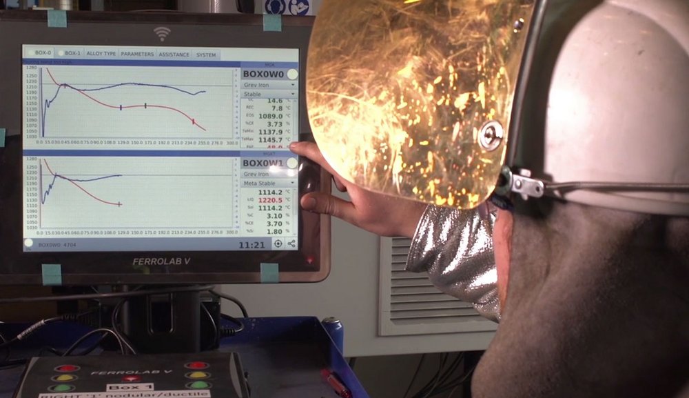 Foundry worker analyzing temperature data on a digital screen during metal casting process.