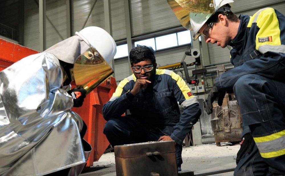 Three foundry workers in protective gear inspecting a 3D-printed filter during a quality check at a STELEX Optiflow facility