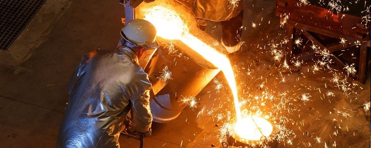 A foundry worker in protective gear pouring molten metal into a mold, with sparks flying around.