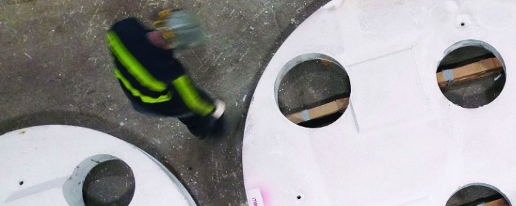 A worker inspecting large refractory steel slabs with circular cut-outs on a factory floor.