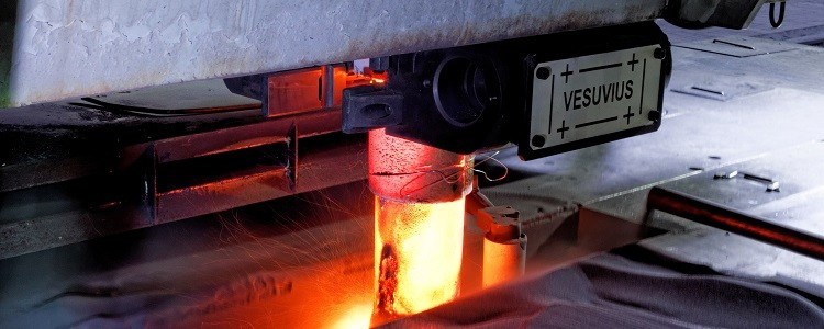 Close-up of a high-temperature steel flow control system with glowing molten steel, labeled 'VESUVIUS', indicative of cutting-edge metallurgical technology.